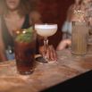 Crop multiethnic girlfriends at counter with assorted cocktails in bar