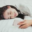 Smiling woman texting on cell phone on bed