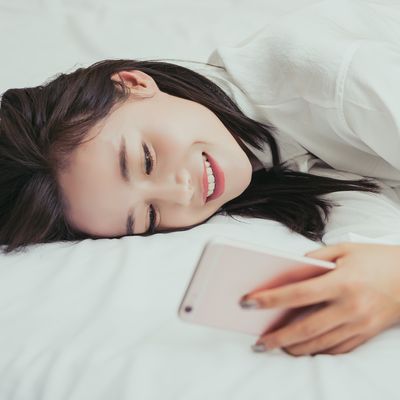 Smiling woman texting on cell phone on bed