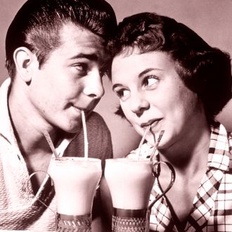 1940s 1950s romantic teenage couple boy and girl head to head drinking ice cream sodas