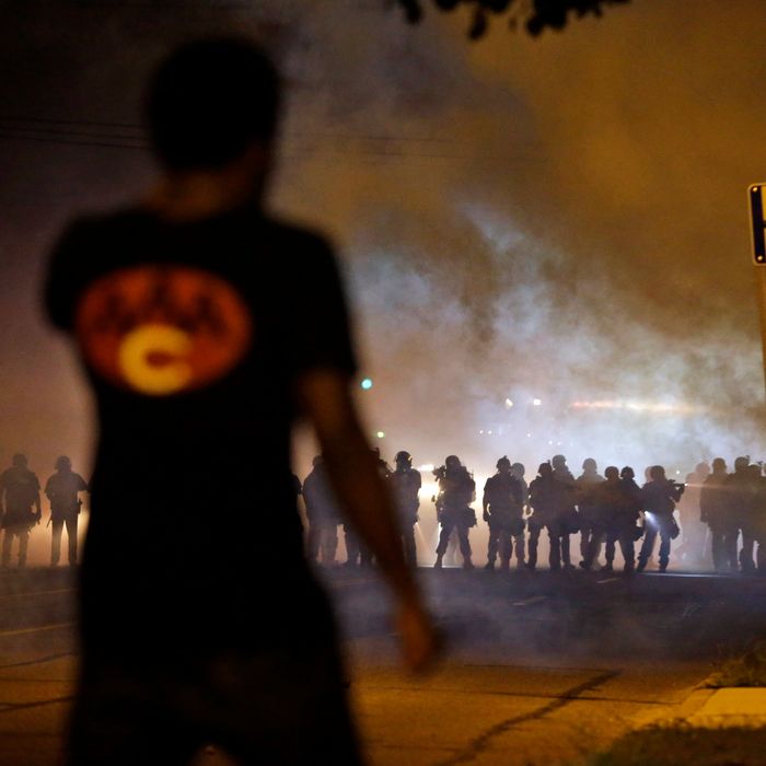A man watches as police walk through a cloud of smoke during a clash with protesters Wednesday, Aug. 13, 2014, in Ferguson, Mo. Protests in the St. Louis suburb rocked by racial unrest since a white police officer shot an unarmed black teenager to death turned violent Wednesday night, with people lobbing Molotov cocktails at police who responded with smoke bombs and tear gas to disperse the crowd. (AP Photo/Jeff Roberson)