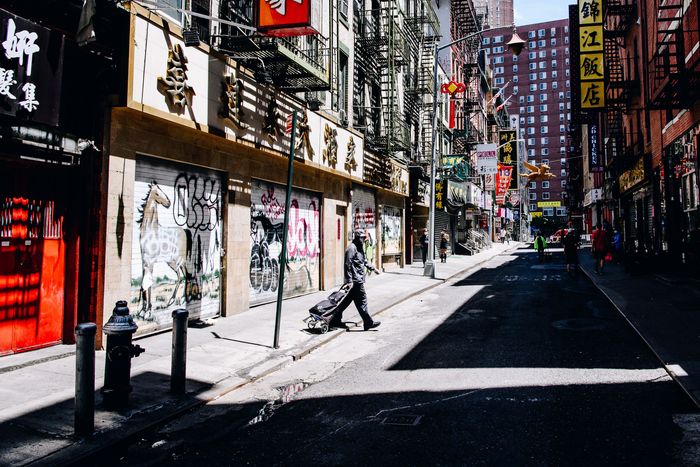 a street in Chinatown with closed storefronts, a single pedestrian crossing the street.