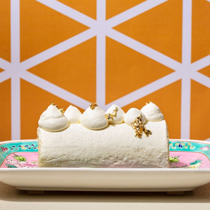 A Swiss roll cake with white frosting against an orange-and-white geometric background.