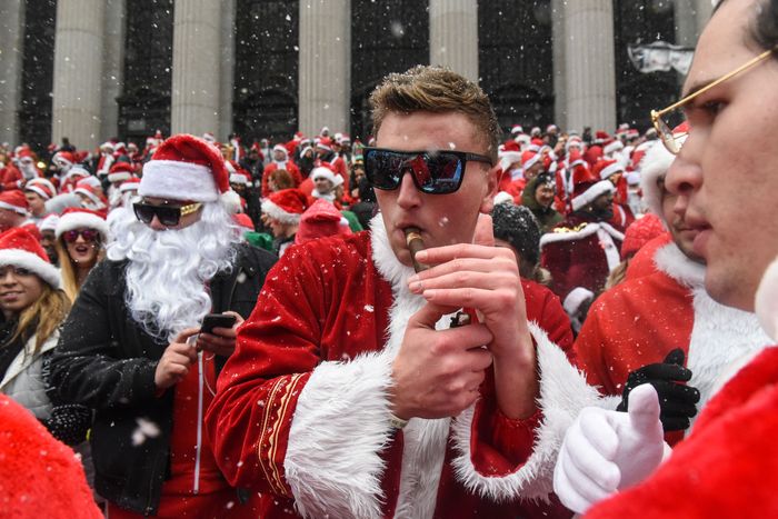 A young blond man wearing sunglasses, wearing a Santa suit, and smoking a cigar at SantaCon NYC