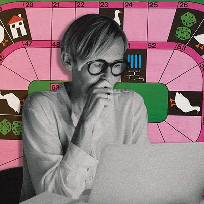 A woman with cropped blonde hair and thick-rimmed black glasses stares down at a laptop computer screen. Her right hand covers her mouth in concentration.