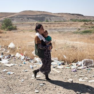 10 Aug 2014, Sinjar, Iraq --- FISHKHABOUR, IRAQ: A Yezidi woman carries her child to shelter after crossing from Syria back into Iraq. Tens of thousands of Yezidi--an minority ethno-religious group in Iraq--have made there way to safety after being stranded on Mt. Sinjar. They escaped to the mountain after coming under attack by ISIL (The Islamic State of Iraq and the Levant). After days of being stranded, they were able to safely descend the mountain into Syria and then cross back into Iraq further north. --- Image by ? Sebastian Meyer/Sebastian Meyer/Corbis