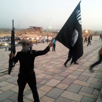 A fighter of the Islamic State of Iraq and the Levant (ISIL) holds an ISIL flag and a weapon on a street in the city of Mosul in this June 23, 2014 file photo.