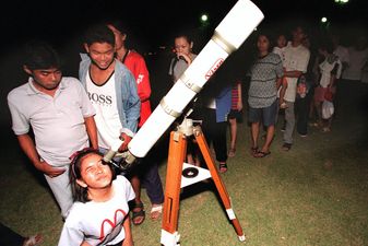 A young stargazer looks through a telescope as oth