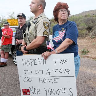 ORACLE, AZ - JULY 15: An anti-immigration activist stands next to a Pinar County Sheriff's deputy during a protest along Mt. Lemmon Road in anticipation of buses carrying illegal immigrants on Jully 15, 2014 in Oracle, Arizona. About 300 protesters lined the road waiting for a busload of illegal immigrants who are to be housed at a facility in Oracle. (Photo by Sandy Huffaker/Getty Images)
