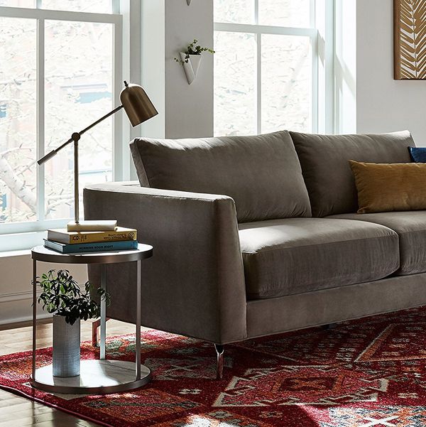A Wayfair large desk lamp on a side table next to a grey couch on top of a dark red patterned rug. The Strategist - Very Tasteful Lamps from Amazon’s Rivet and Stone and Beam Are on Sale