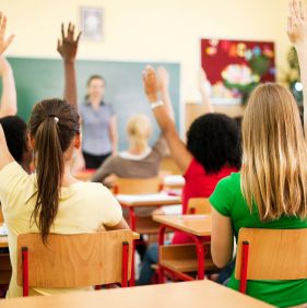 Rear view of the teens sitting in the classroom and raising hands to answer the question.