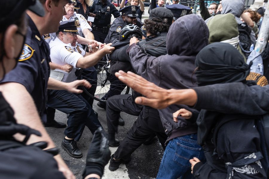 Police officers pull a person away from a group of other protesters in a crowd.
