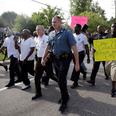 Thousands of demonstrators peacefully march down a street with members of the St. Louis County Police and Missouri Highway Patrol Thursday, Aug. 14, 2014, in Ferguson, Mo. The Missouri Highway Patrol seized control of a St. Louis suburb Thursday, stripping local police of their law-enforcement authority after four days of clashes between officers in riot gear and furious crowds protesting the death of an unarmed black teen shot by an officer. (AP Photo/Jeff Roberson)