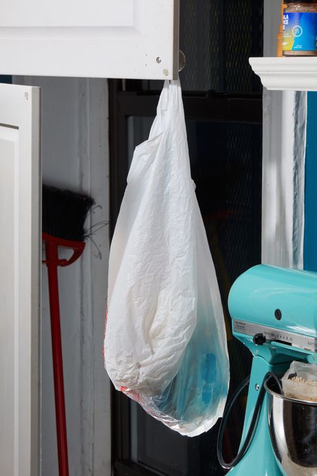 A plastic bag hanging from a cabinet next to a blue KitchenAid stand mixer