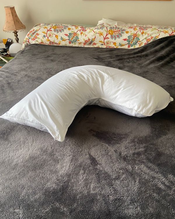 A white boomerang-shaped pillow on a bed.