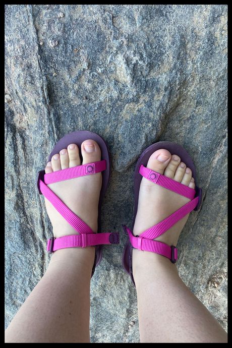 A photo of a person's feet wearing pink sandals on rock.