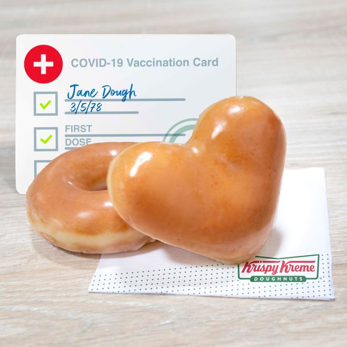 A Covid-19 vaccine card with two Krispy Kreme glazed doughnuts in front of it, one shaped like a heart.
