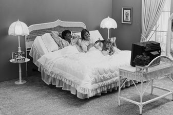 Father and mother with daughter lying on bed watching tv, smiling