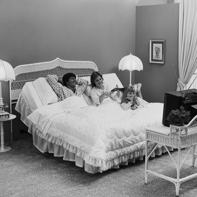 Father and mother with daughter lying on bed watching tv, smiling