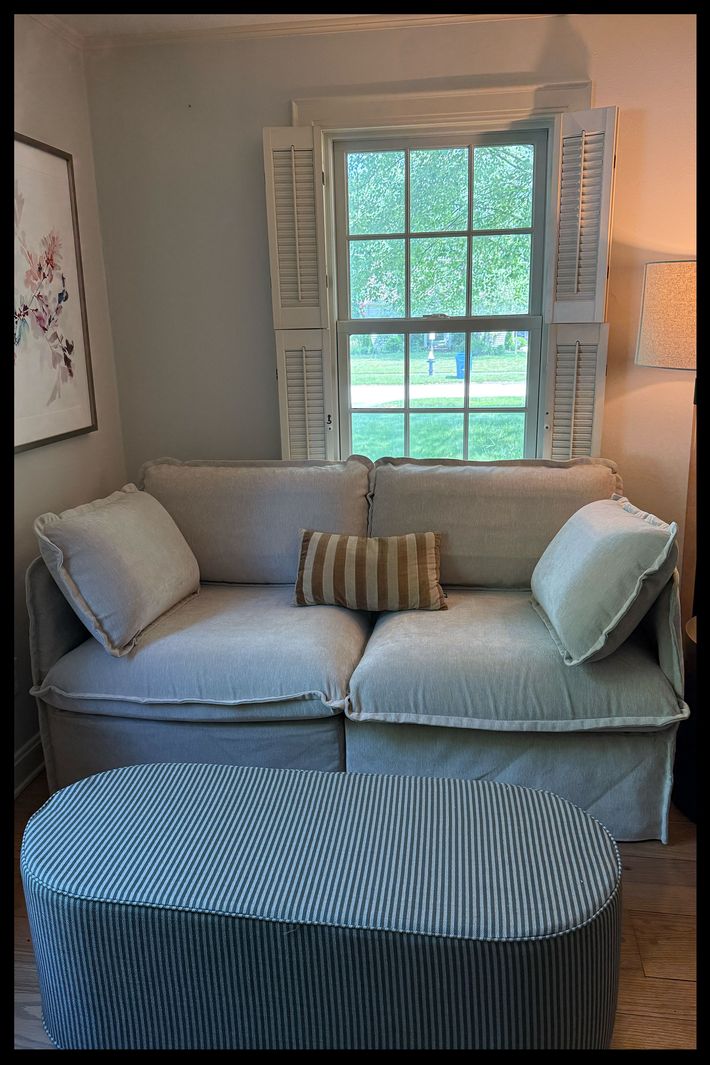 A striped pill-shaped fabric coffee table in front of a loveseat.