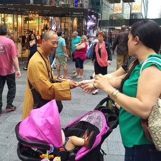 In this June 23, 2016 photo, a man who says he is a Buddhist monk hands a medallion to a woman as he solicits donations on New York City's Times Square. Leaders of New York City's Buddhist community said that men in orange robes seeking donations near New York's popular tourist attractions are fakes, posing as monks to trick people into giving up their money. (AP Photo/Michael Balsamo)