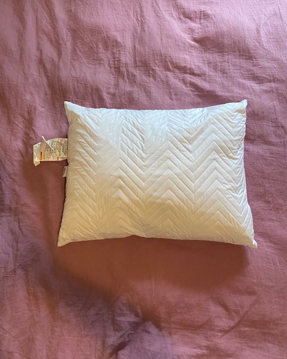 A white pillow on a pink duvet.