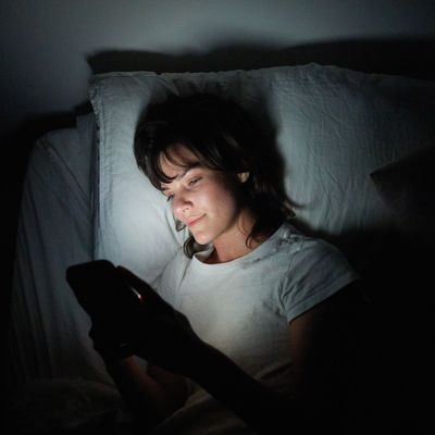 Young woman using her cellphone while lying in bed at night