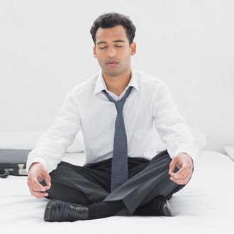 Relaxed young businessman sitting in lotus pose on bed