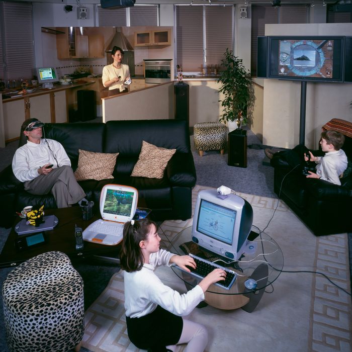 A family sits around a living room. Each person is looking at a computer.