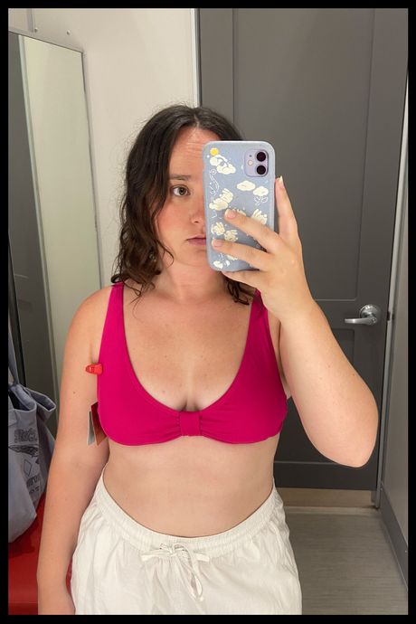 A person wearing a pink swimsuit top in a dressing room.