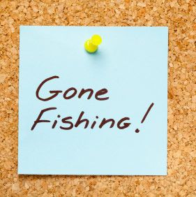 GONE FISHING! written on a blue sticky note on an office cork bulletin board.